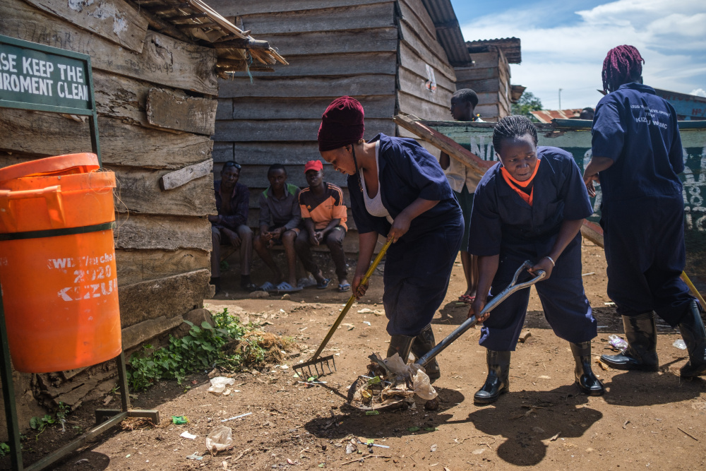Frauen harken sandigen Boden neben Holzgebäuden