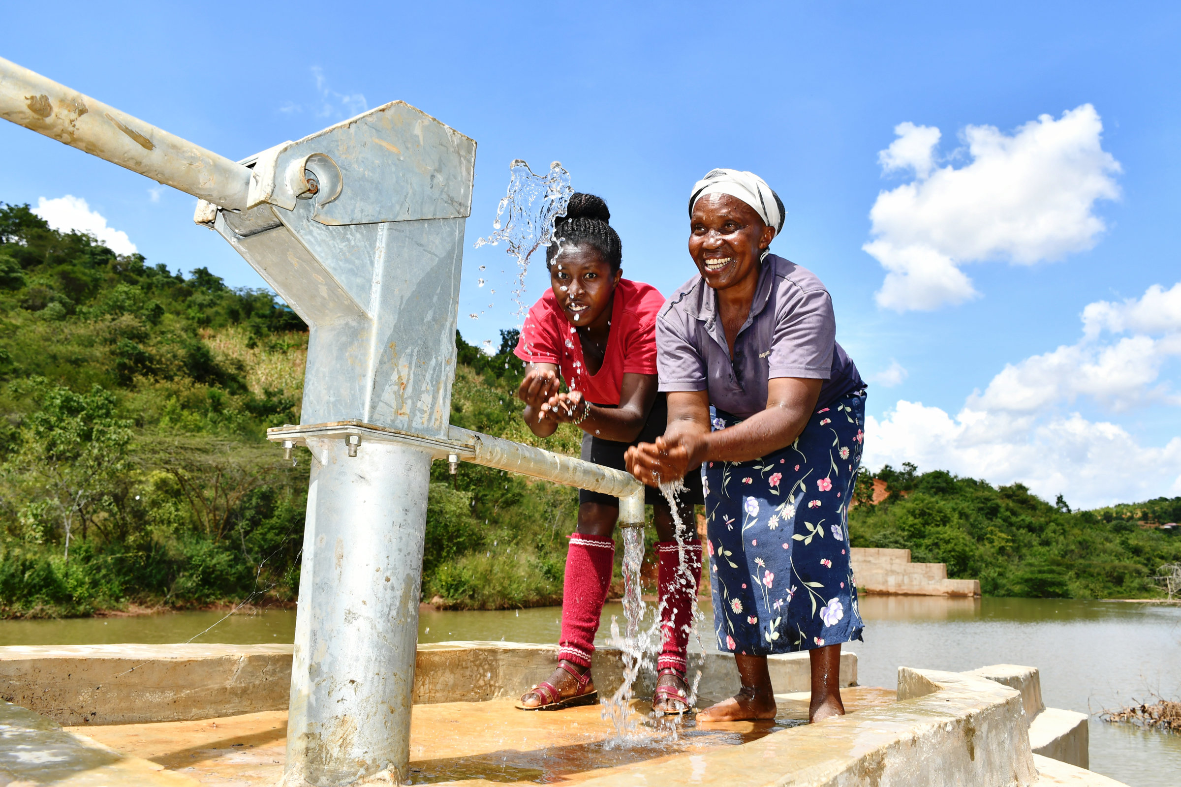Zwei Frauen an einer Handpumpe fangen das Wasser mit Händen auf